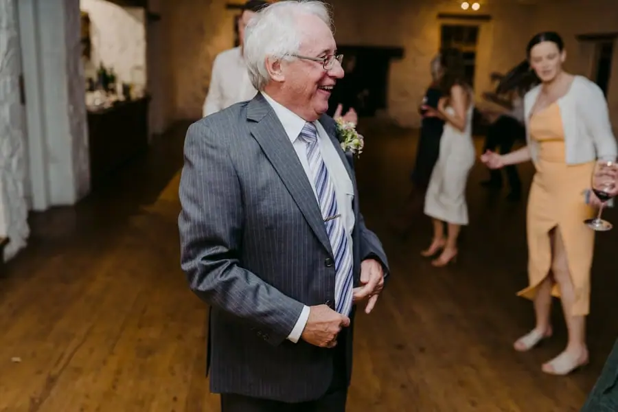 Older man laughing while dancing in a stone-walled room
