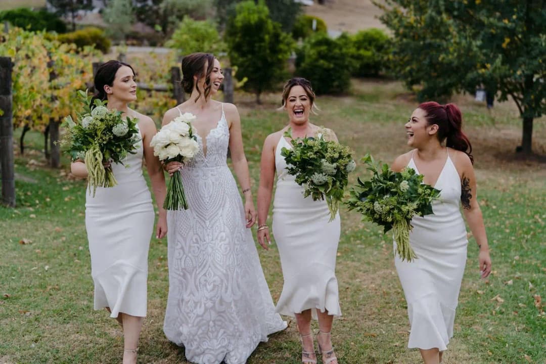 Bride and three bridesmaids laughing as they walk across a lawn with bouquets