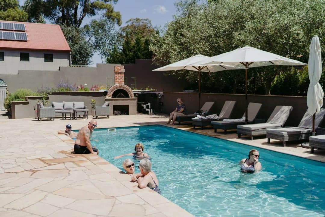 Guests relaxing in an outdoor swimming pool beside loungers and a large umbrella