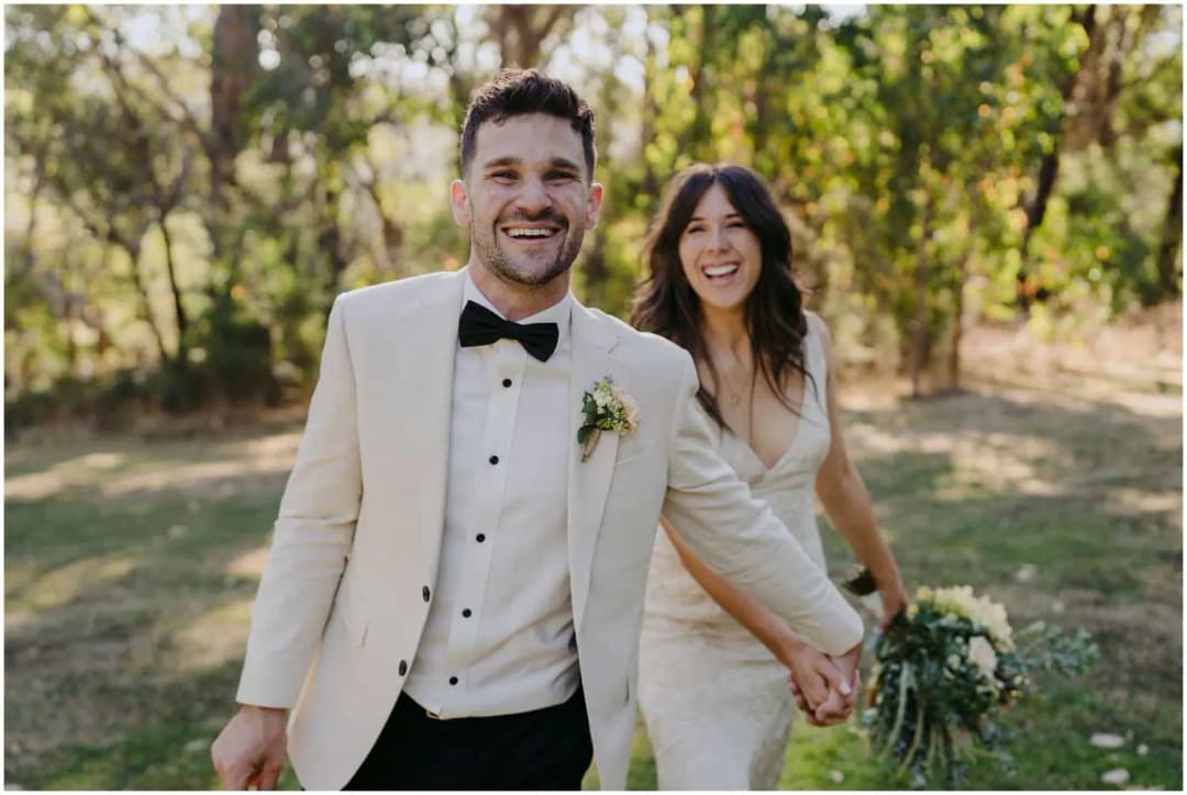Bride and groom smiling and holding hands in a wooded garden.