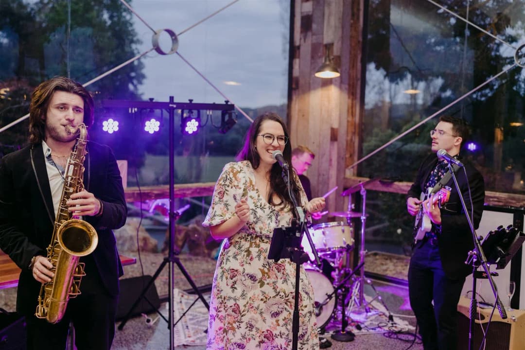 Band with a saxophonist and singer performing beneath purple stage lights.
