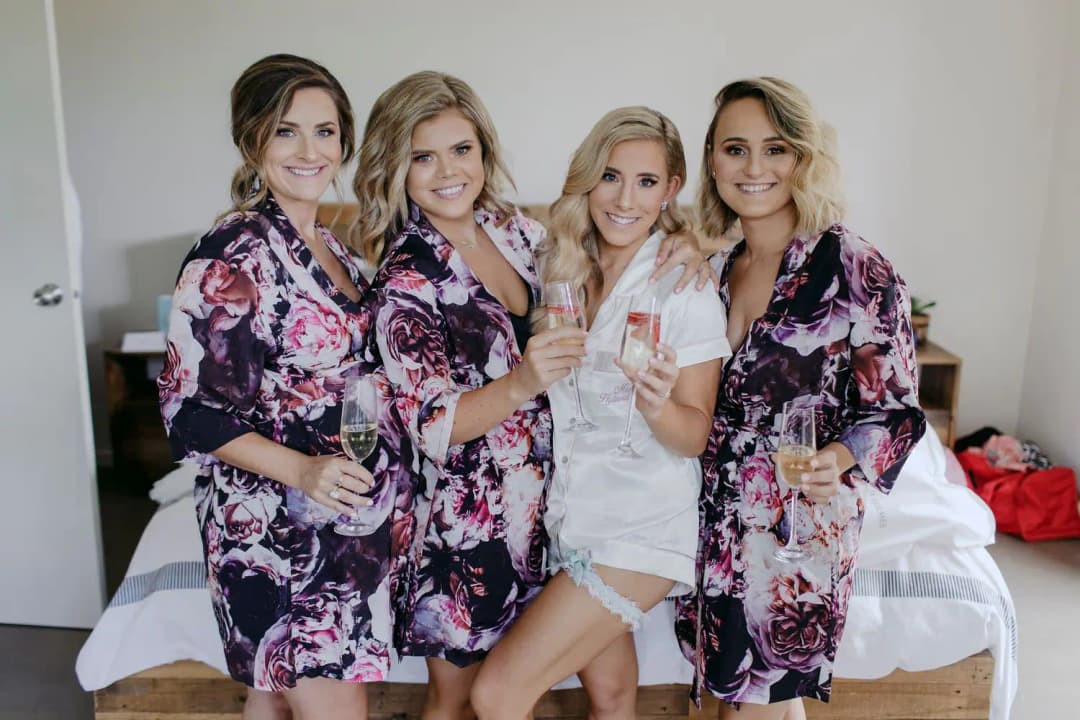 Bride and three friends smiling with drinks while wearing floral robes