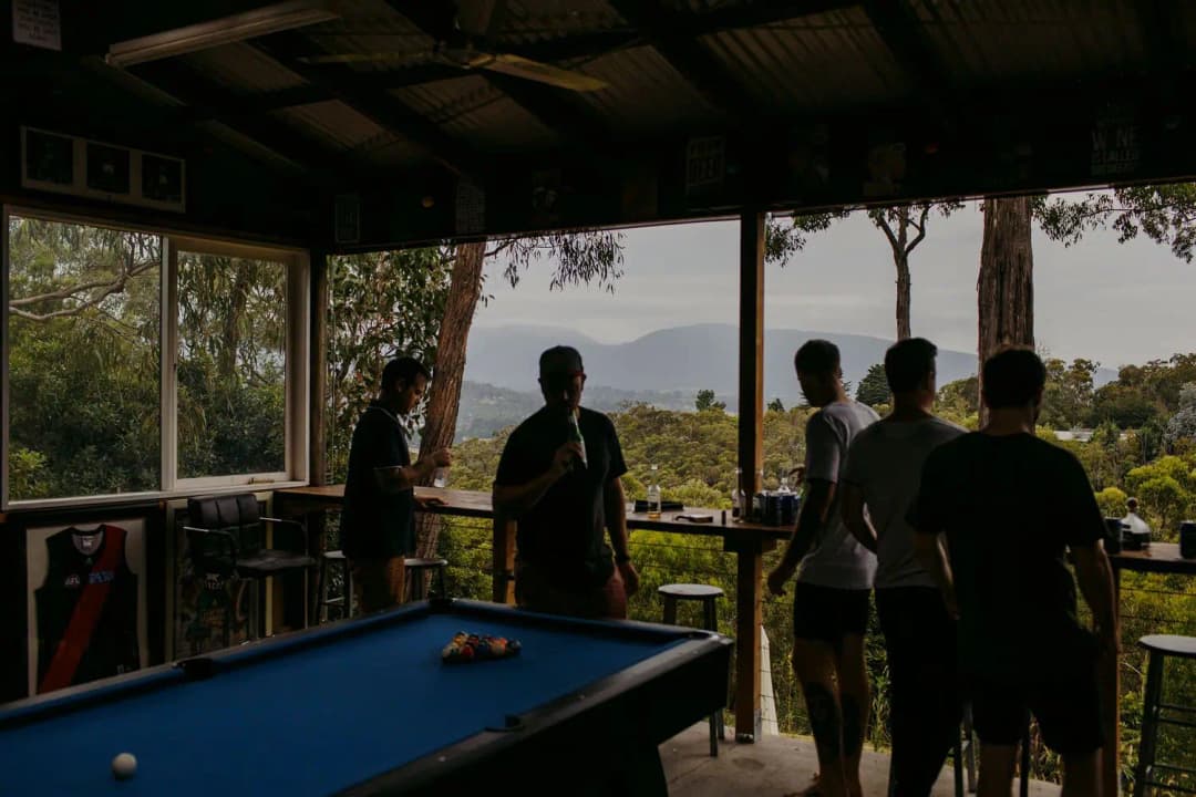 Men gathered beside a pool table on a covered veranda overlooking hills