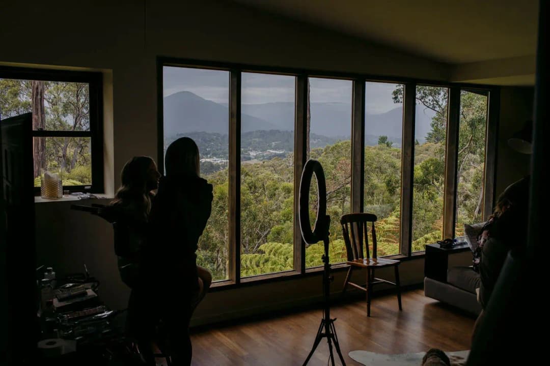 Silhouettes of women getting ready beside large windows overlooking hills
