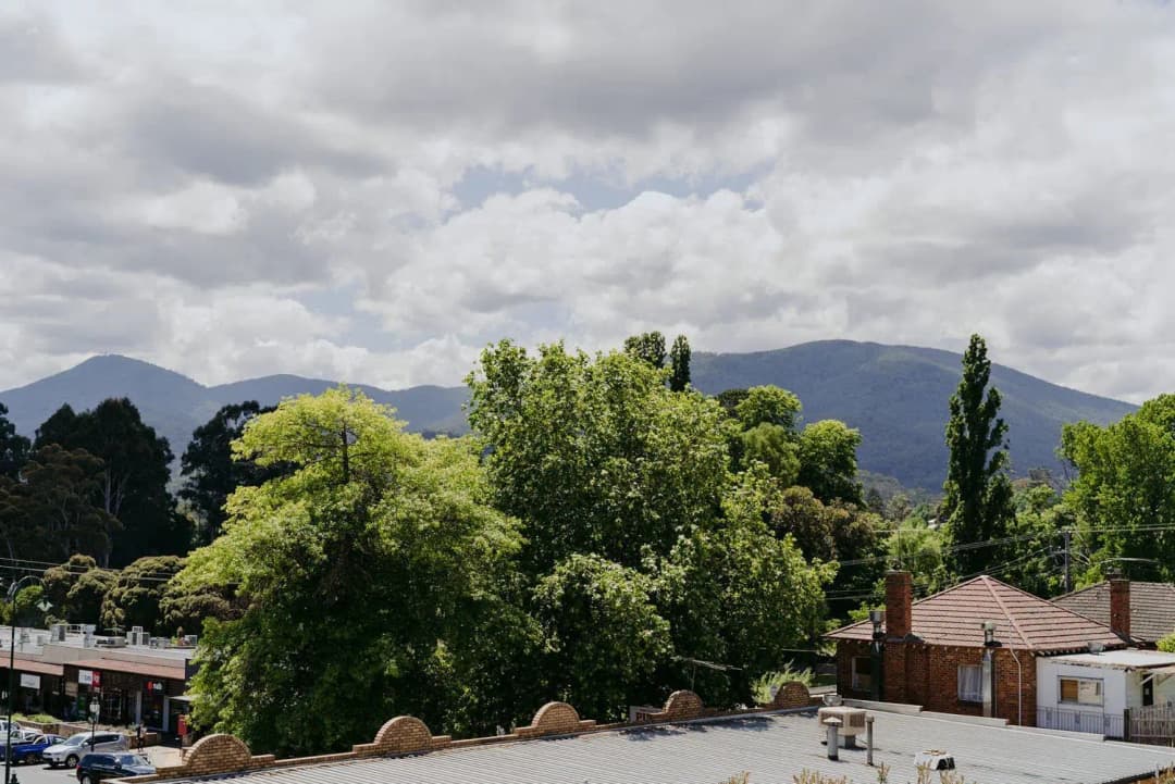Town rooftops and leafy trees beneath a cloudy mountain backdrop