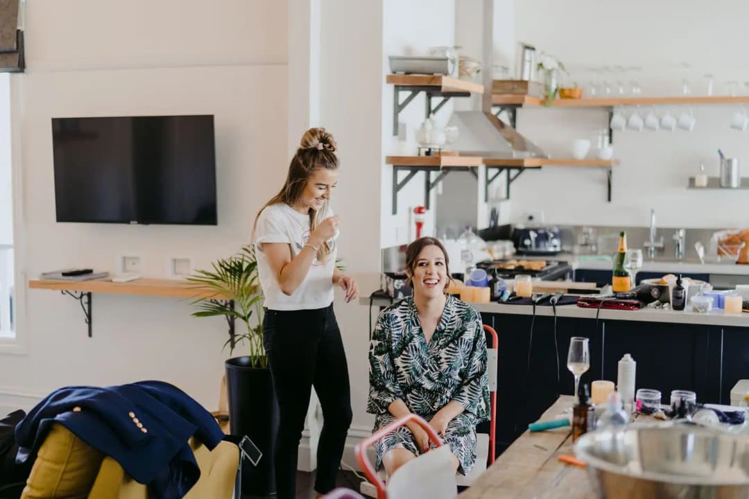 Women laughing while getting ready in a bright living room and kitchen