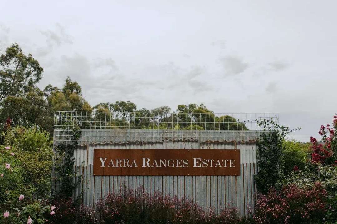 Rust-coloured estate sign mounted on a corrugated structure beside flowering plants.