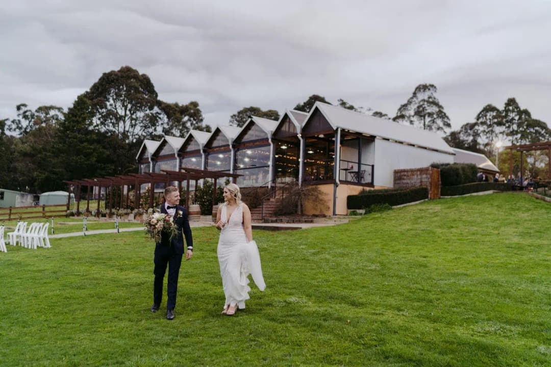 Bride and groom walking down a lawn in front of a building with multiple gabled roofs.