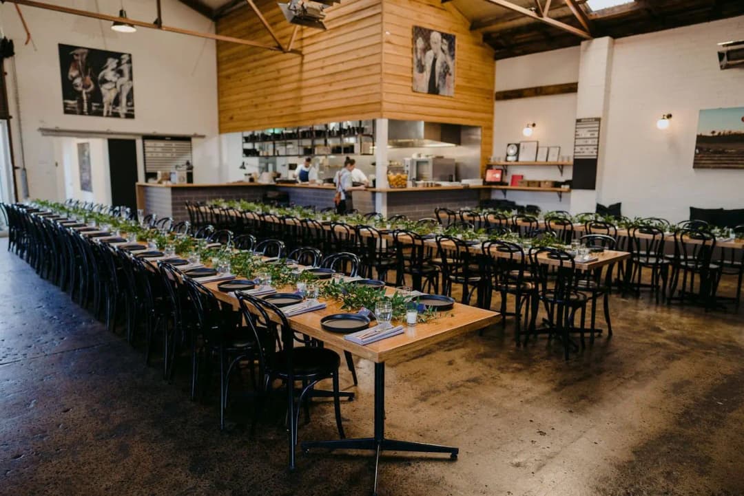 Long wooden reception tables and dark chairs beneath exposed roof beams.