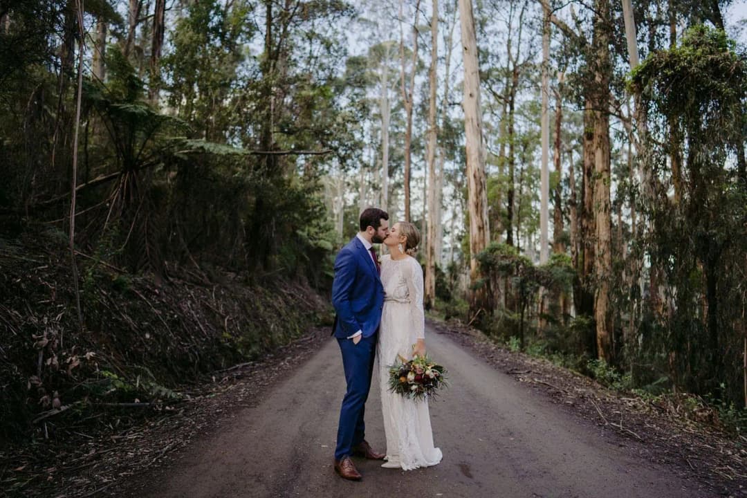 Couple embracing on a quiet road through tall forest trees.