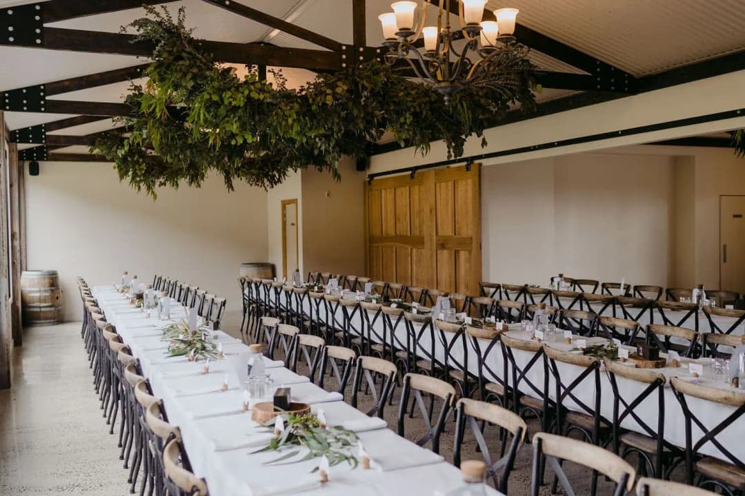 Long white reception tables beneath chandeliers and hanging greenery.