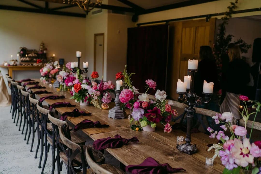 Long wooden reception table decorated with pink flowers and candles.