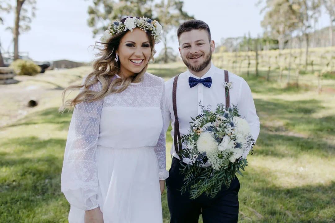 Bride and groom smiling together on a lawn with a white and green bouquet.