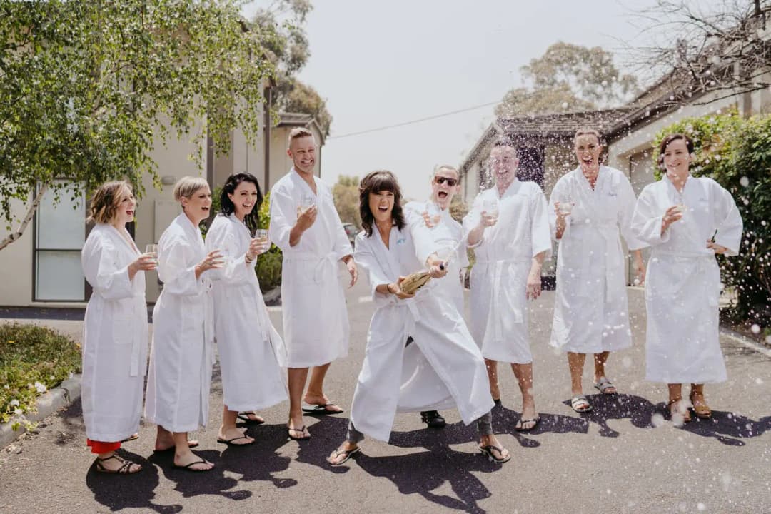 Wedding party laughing outdoors while dressed in white robes