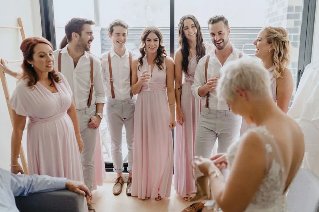 Wedding party in pale outfits smiling at the bride indoors