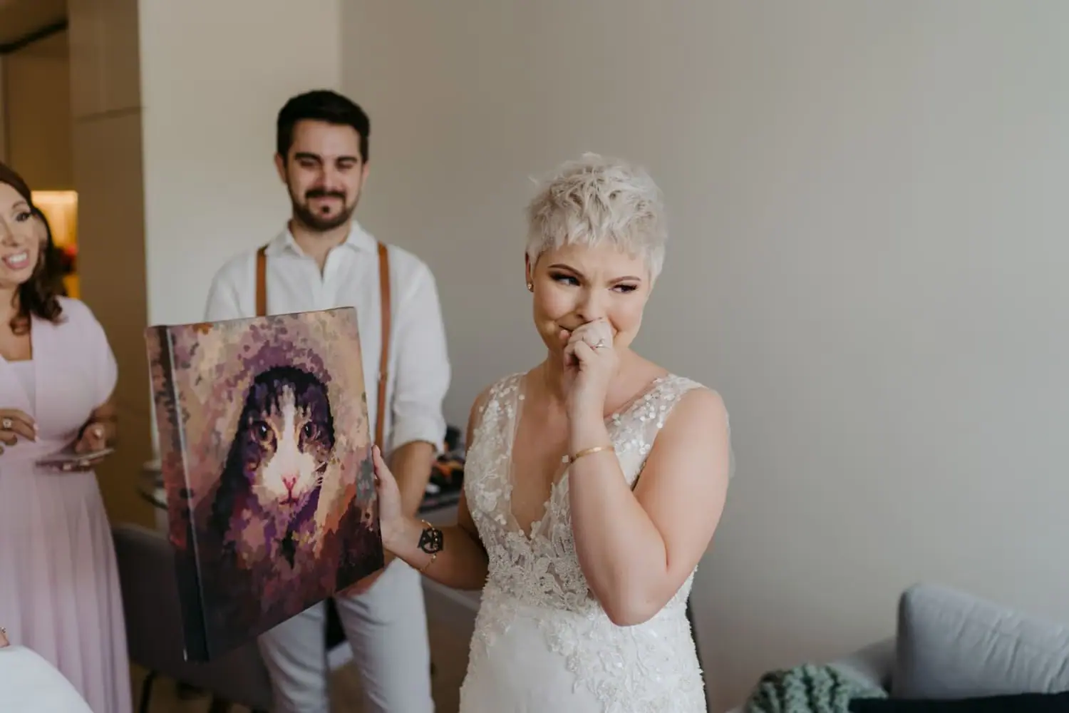 Bride smiling with a hand to her face as a guest holds an artwork