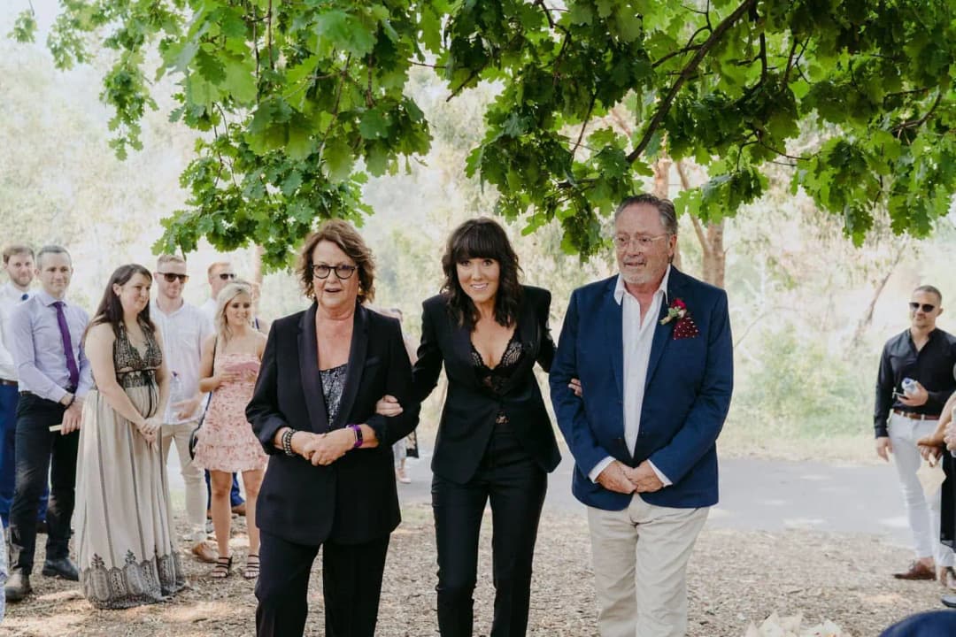 Bride walking arm in arm with two older guests toward the ceremony