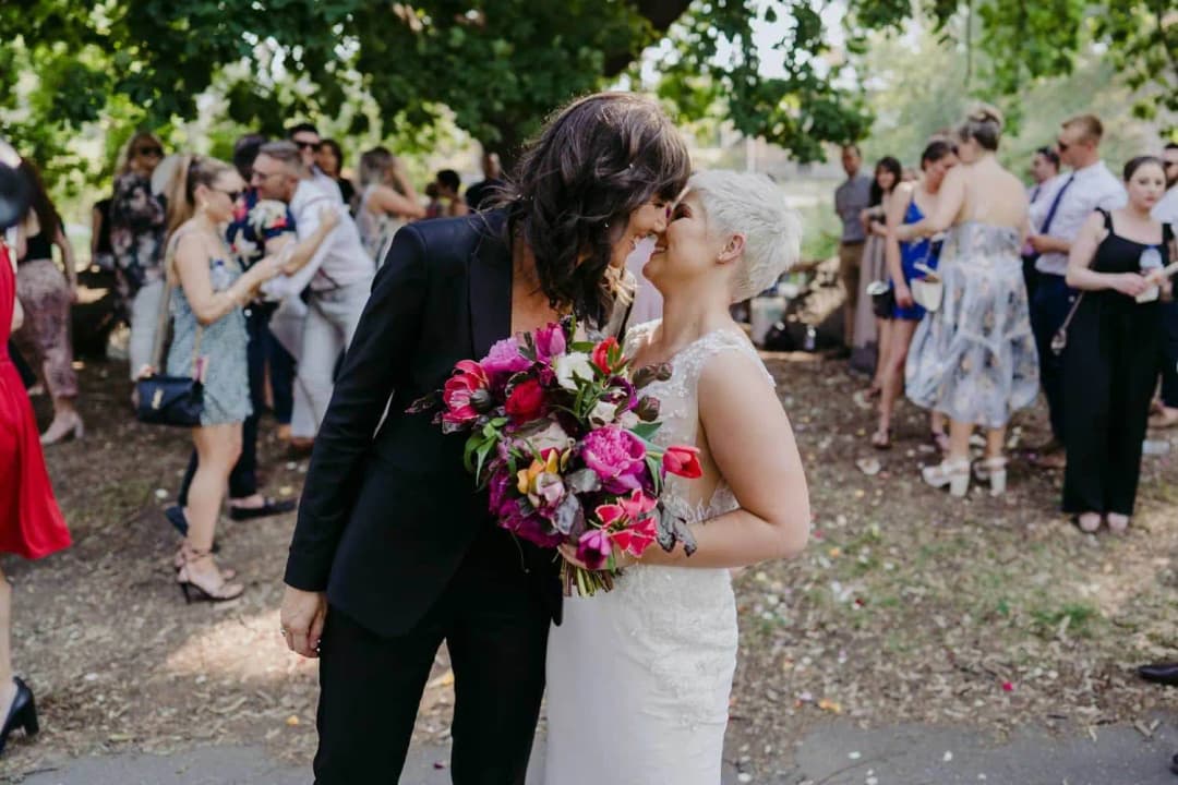 Newlyweds kissing while holding a bright pink bouquet