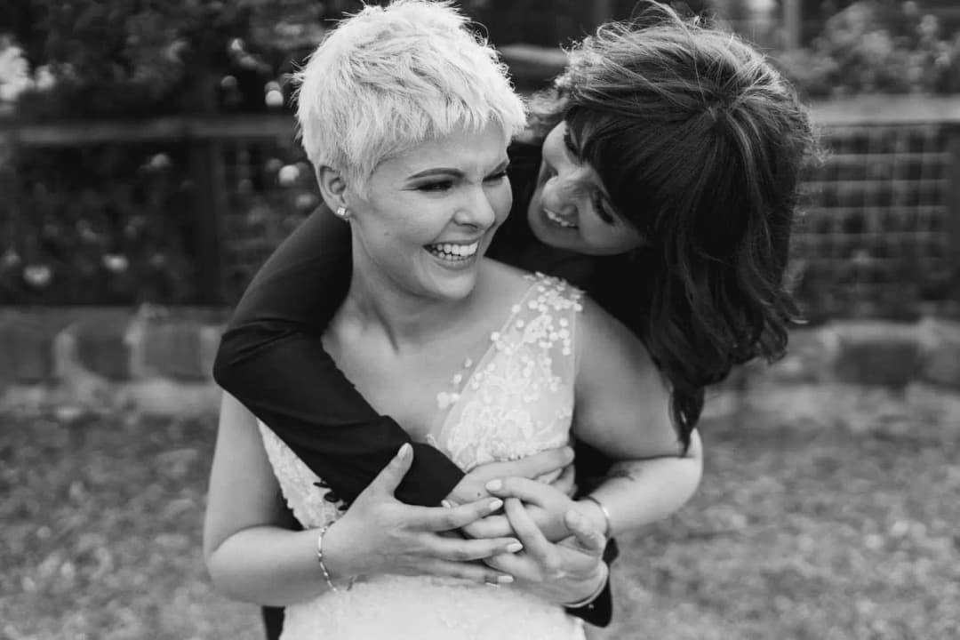 Black-and-white photograph of one bride embracing her partner from behind
