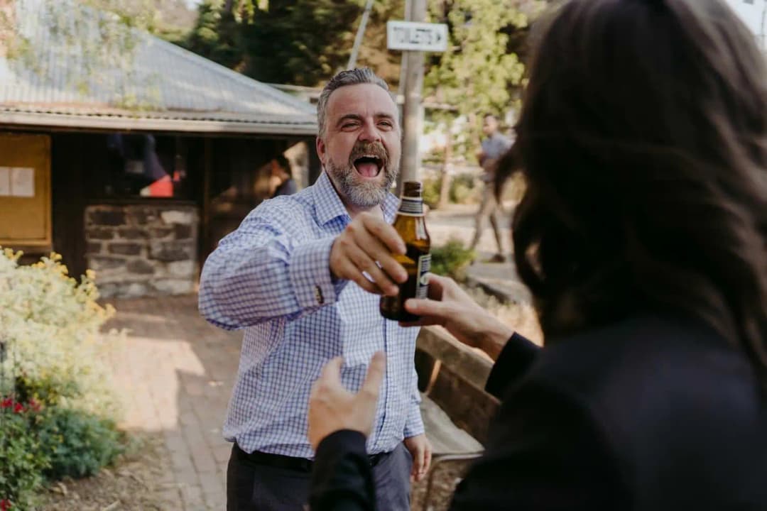 Guest raising a bottle while laughing outside the reception barn