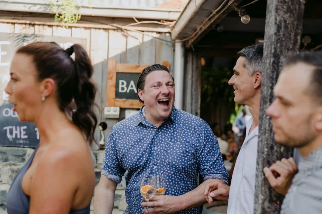 Guests laughing with drinks outside the reception barn