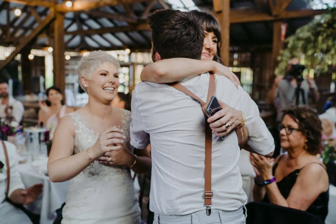 Bride smiling as her partner embraces a guest at the reception