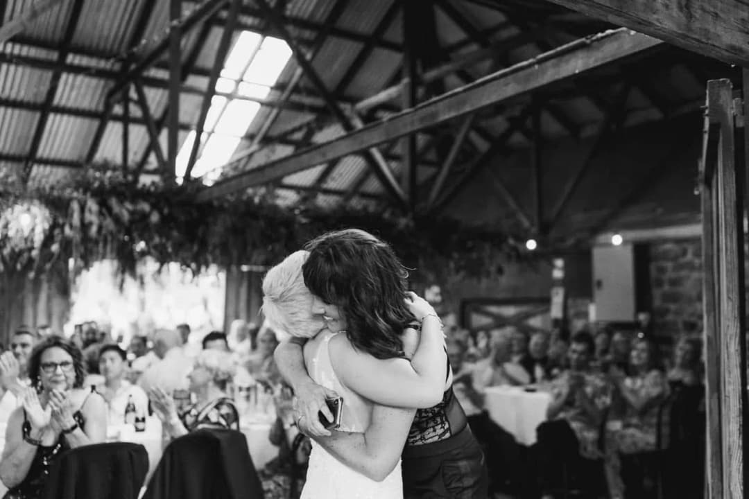 Black-and-white photograph of the couple embracing as guests watch