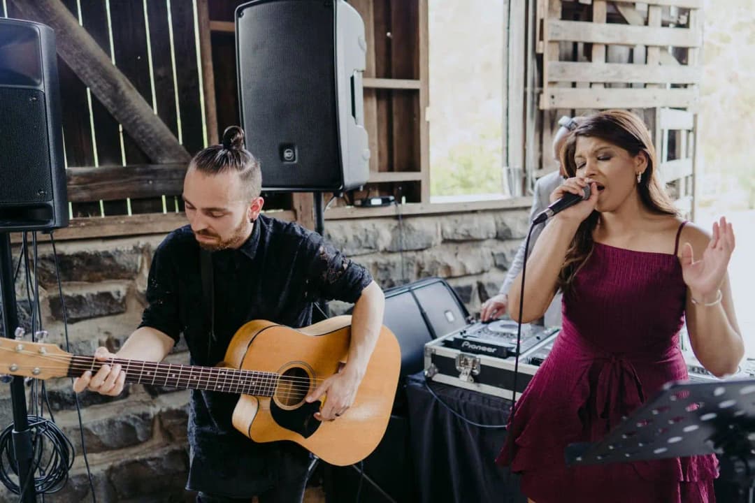 Singer performing beside an acoustic guitarist inside the barn