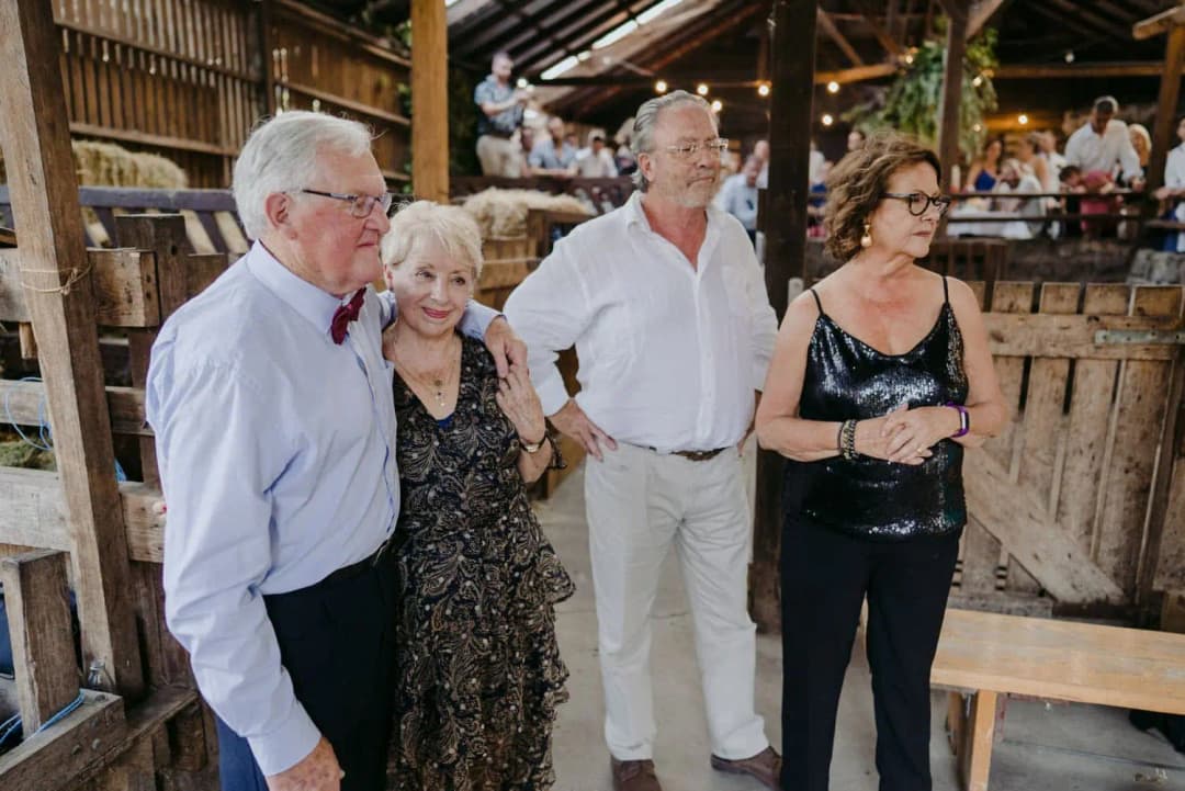 Four guests smiling together beside a wooden barn railing