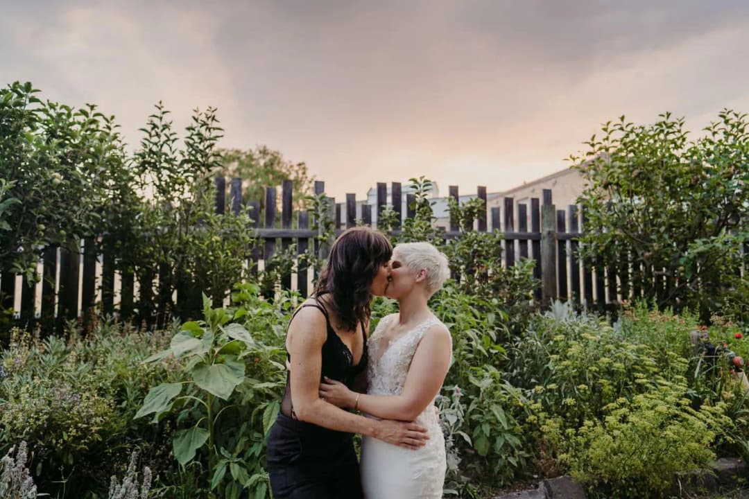 Couple kissing beside a garden fence beneath a soft evening sky