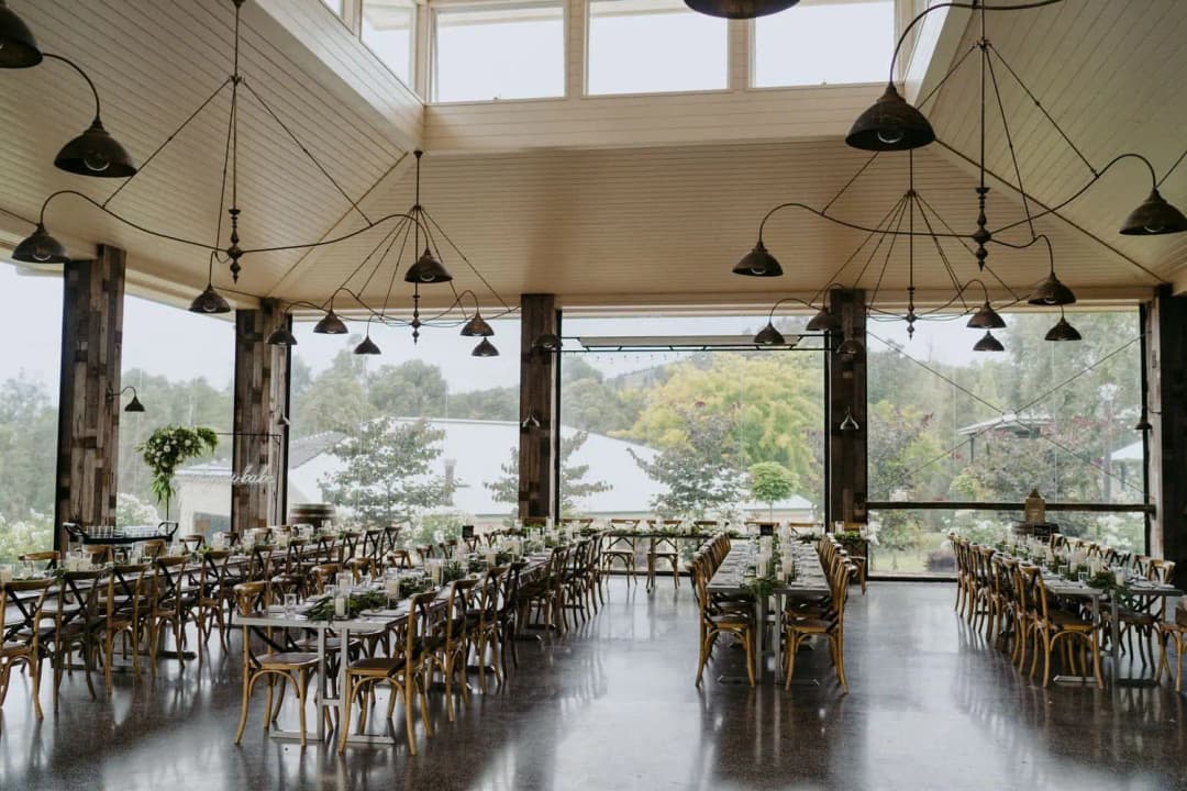 Rows of reception tables and wooden chairs beneath pendant lights and tall windows