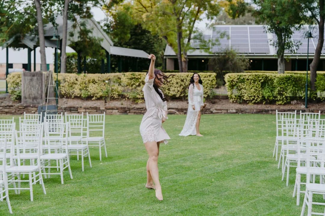 Woman raising one arm while walking between rows of white ceremony chairs