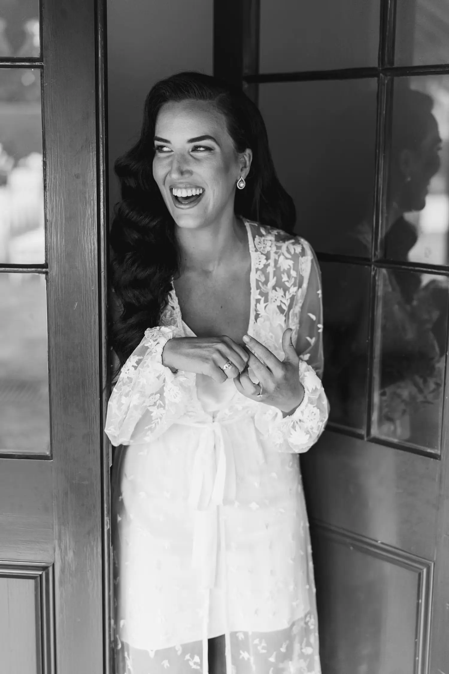 Black and white photograph of a smiling woman holding a glass in a doorway