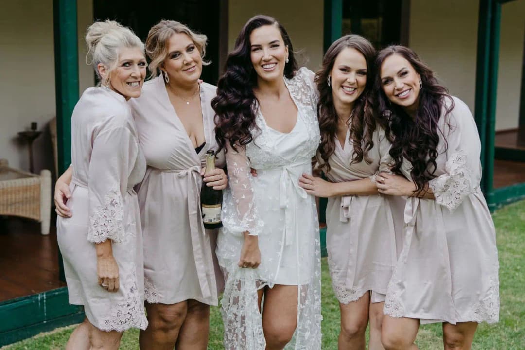 Bride and four women in pale robes smiling together outside green doors