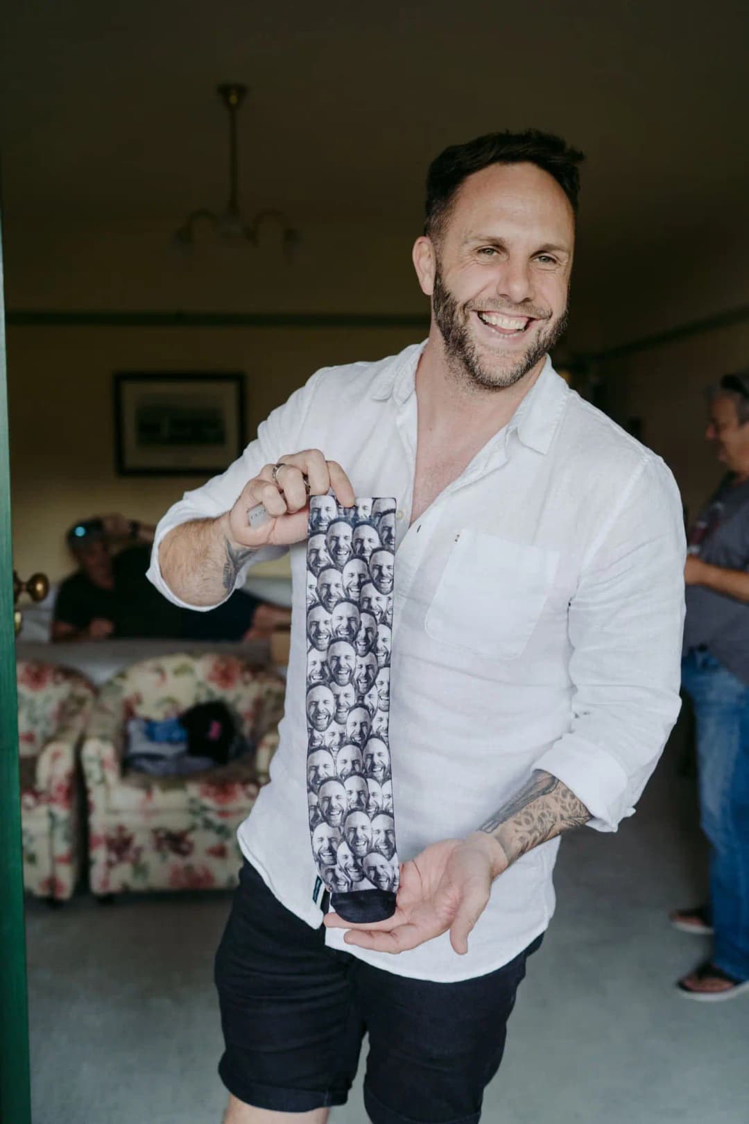 Groom smiling while holding a patterned tie in a bedroom