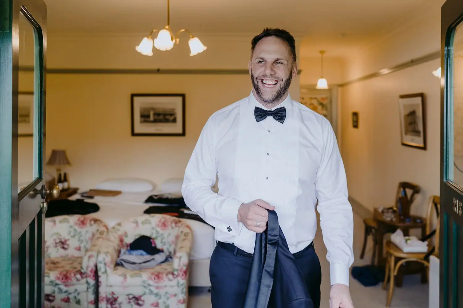 Groom smiling in a white shirt and black bow tie while holding his jacket