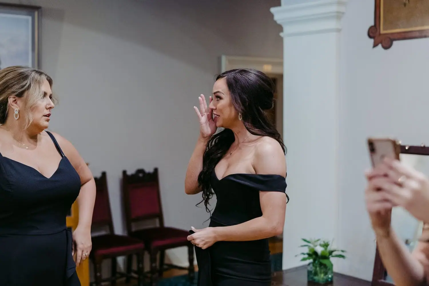 Woman in a black dress wiping her eye while talking with another woman
