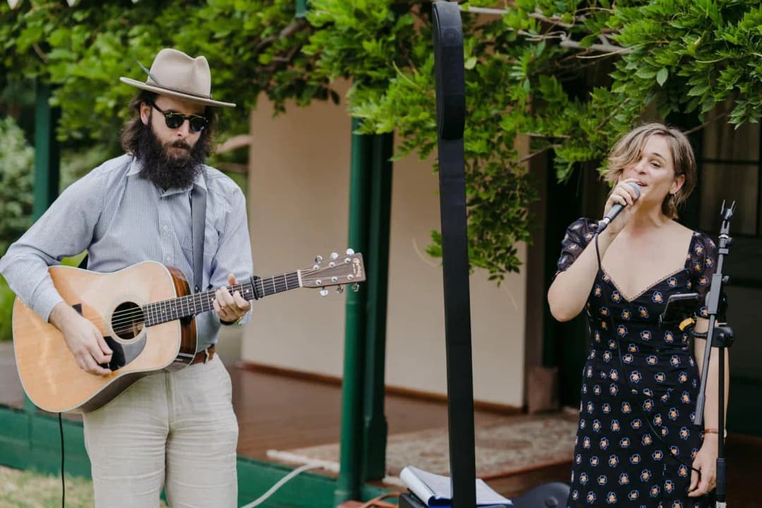 Guitarist in a hat accompanying a singer outdoors beside the venue