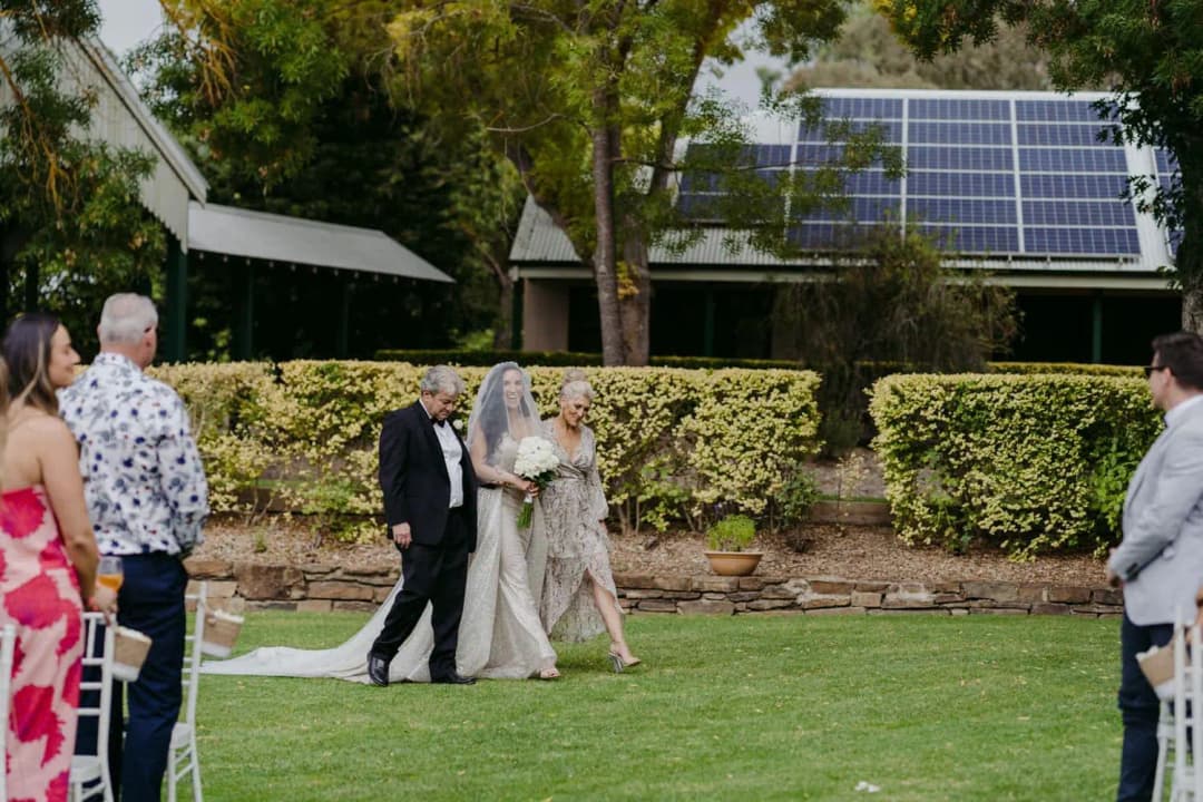 Bride entering the garden ceremony beside a man and woman