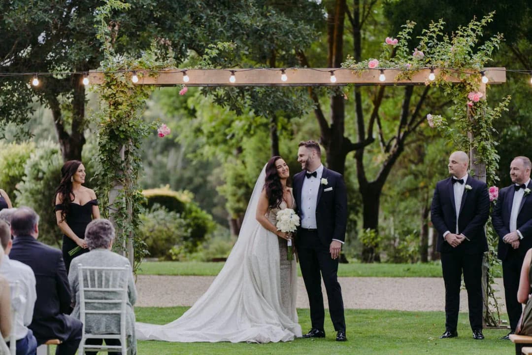 Bride and groom standing beneath a timber floral arch during the ceremony