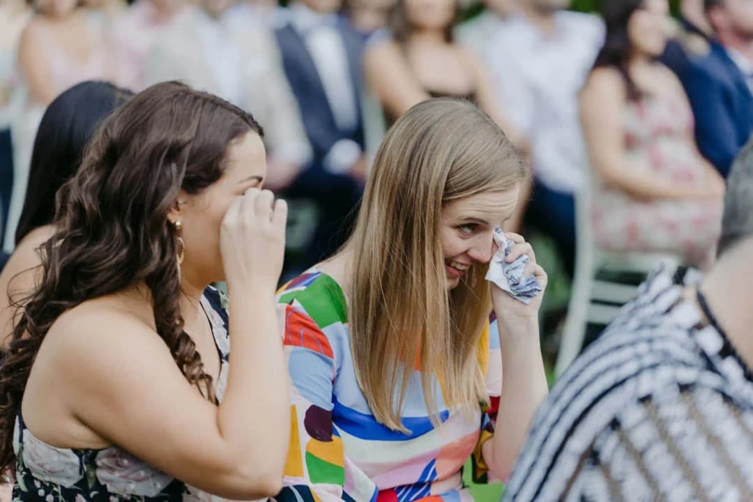 Two seated wedding guests smiling and wiping their eyes during the ceremony
