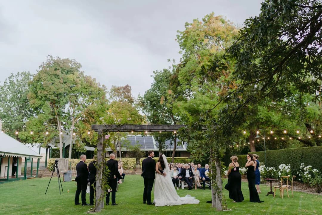 Wide view of the bride and groom beneath a floral arch surrounded by the wedding party