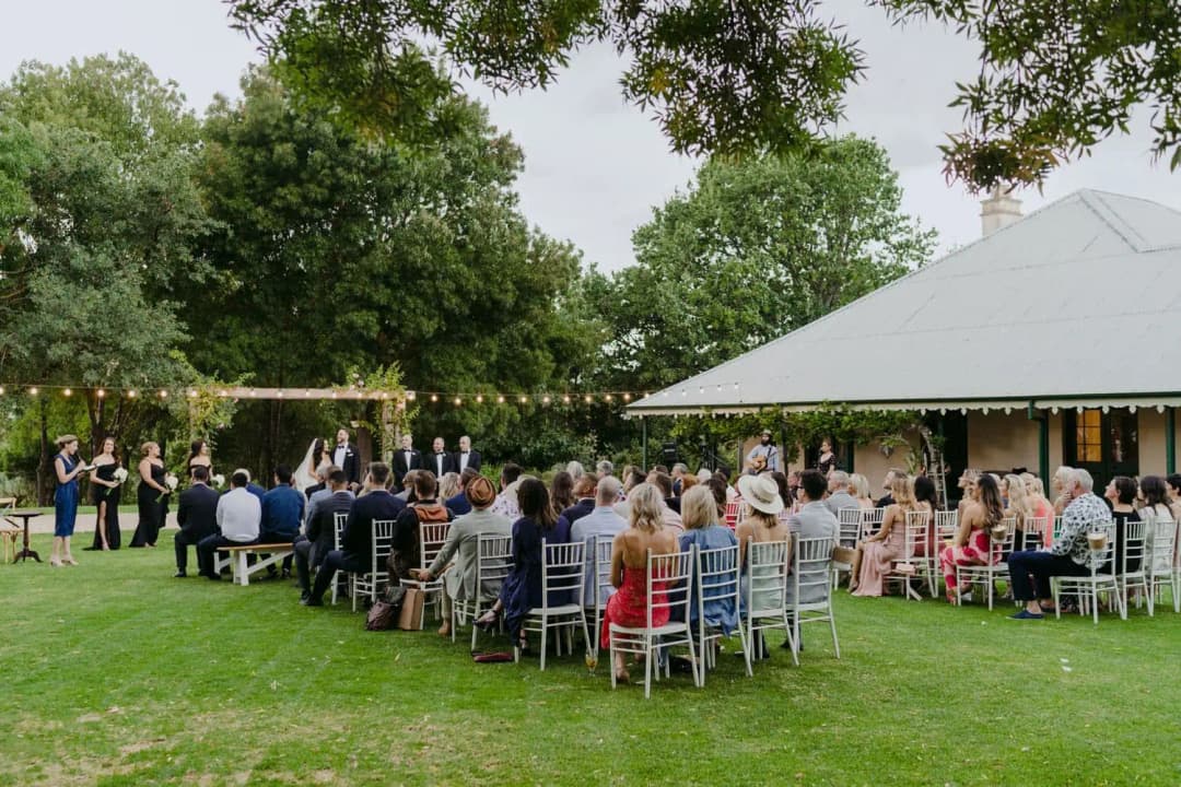 Seated guests watching a ceremony on a lawn beside the venue building