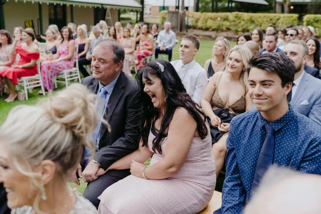 Wedding guests laughing while seated in rows of white chairs