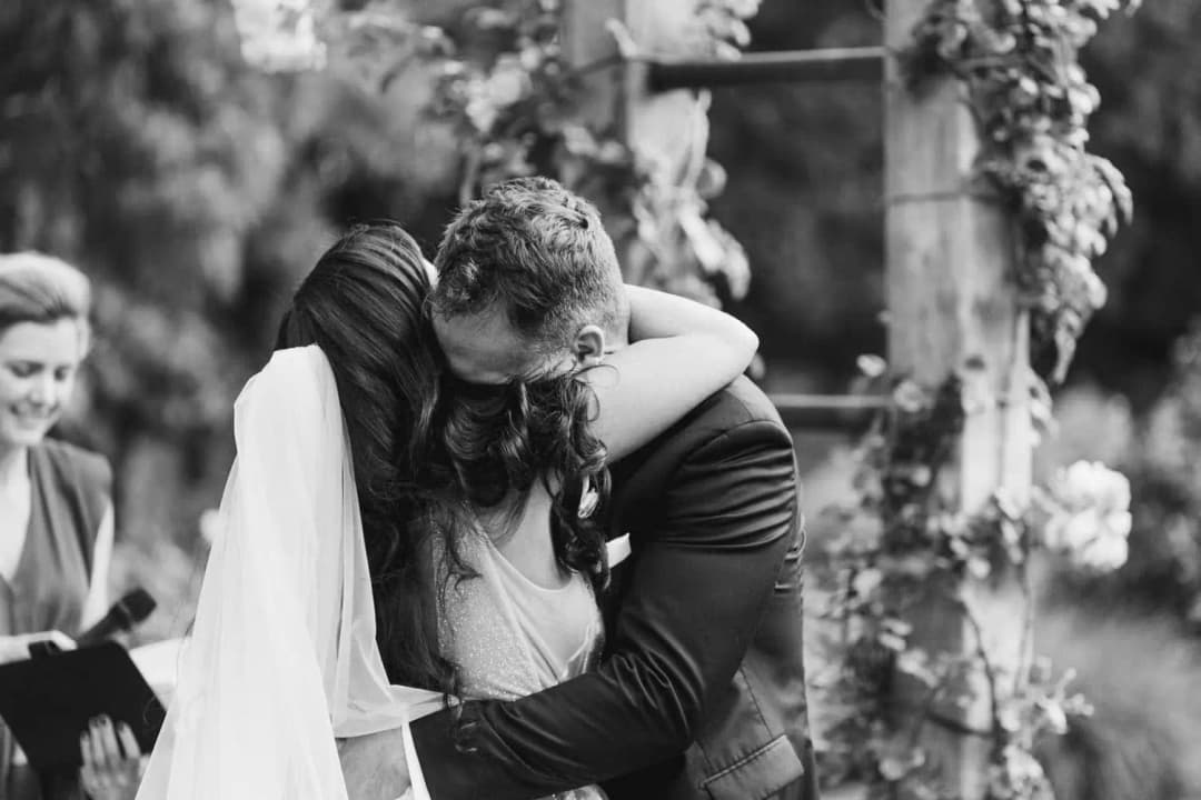 Black and white close-up of the bride and groom embracing beneath the ceremony arch