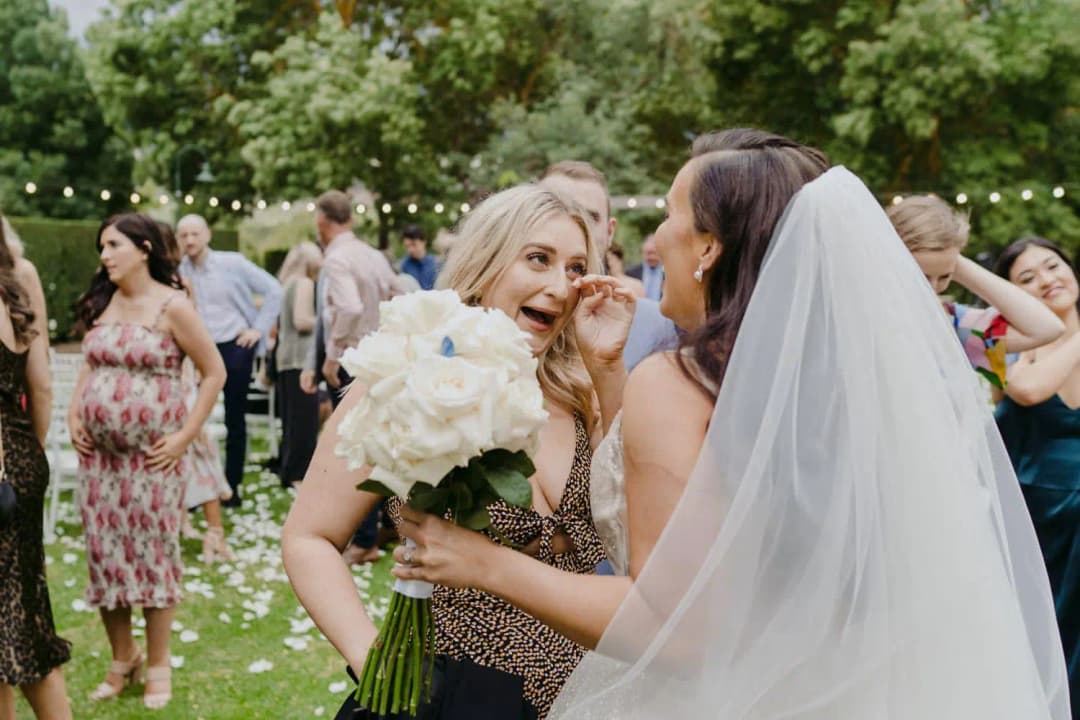 Bride holding her white bouquet while greeting a smiling guest outdoors