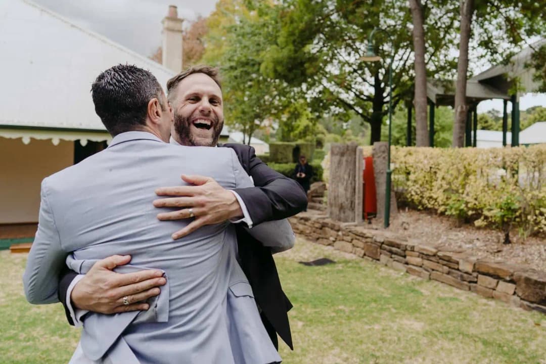 Groom laughing as he hugs a guest in a pale suit outdoors