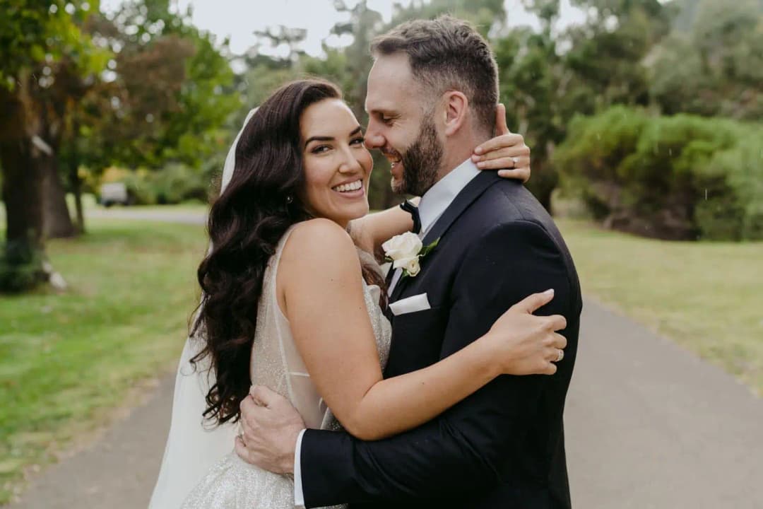 Bride smiling toward the camera as the groom kisses her cheek