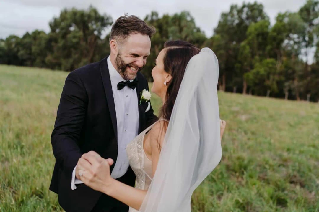 Bride and groom laughing while holding hands in an open field