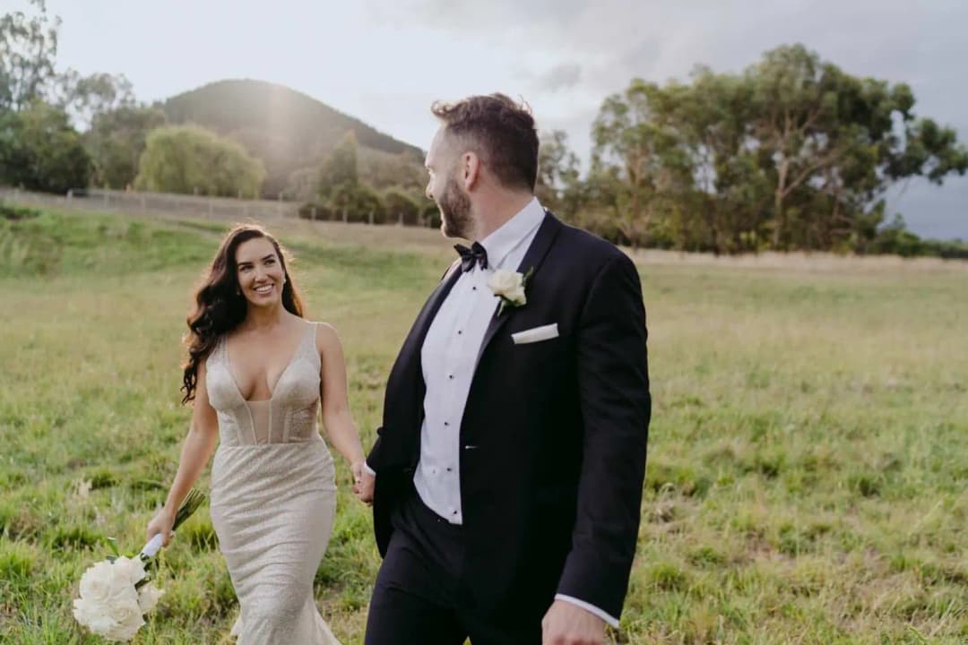 Bride smiling at the groom as they walk through long grass